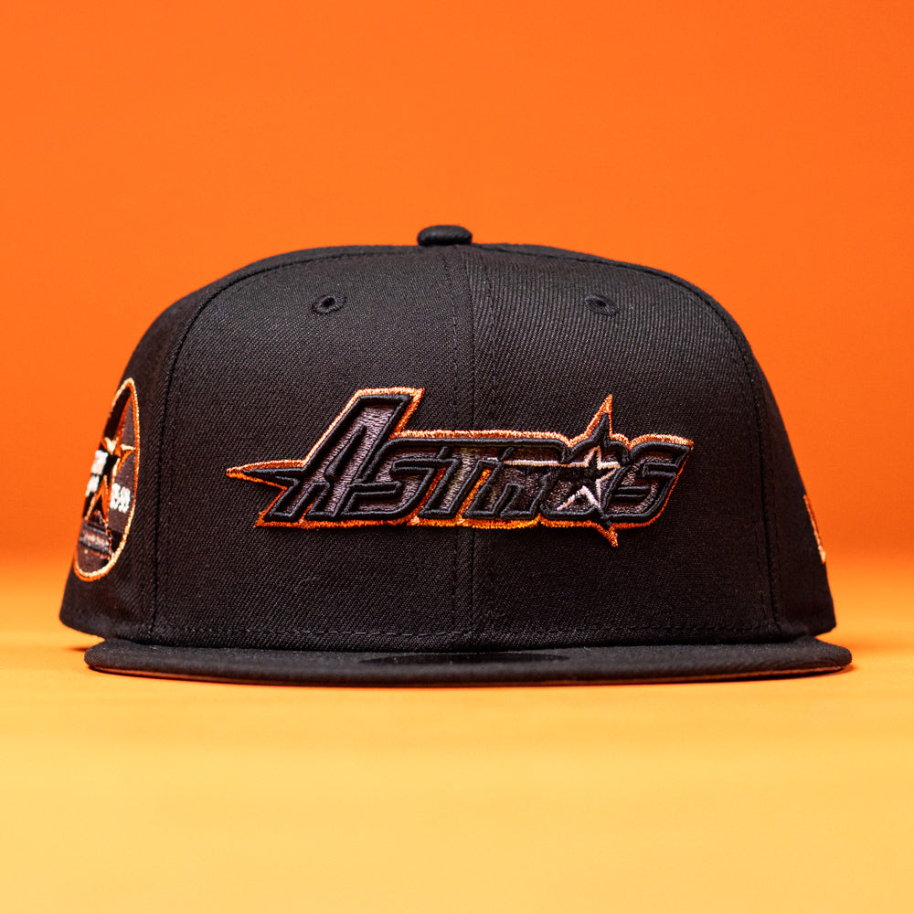 A BLVCK STAR Houston Astros New Era 59FIFTY Fitted Hat in black, featuring the team name embroidered in orange and white on the front, displayed against a solid orange background.