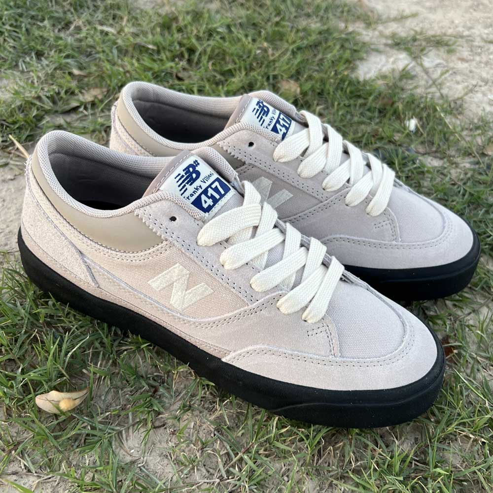 A pair of 417 LSB Franky Villani Grey Black Suede New Balance Numeric skateboarding shoes with white laces and black soles are placed side by side outdoors on grass and dirt.