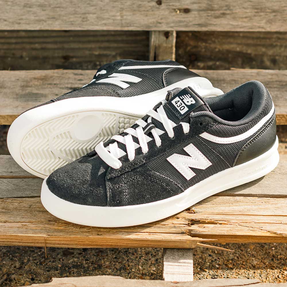A pair of 430 BWH New Balance Numeric Suede Skateboarding Shoes in black and white, featuring “N” logos and cushioned midsoles, rests on a wooden bench outdoors.