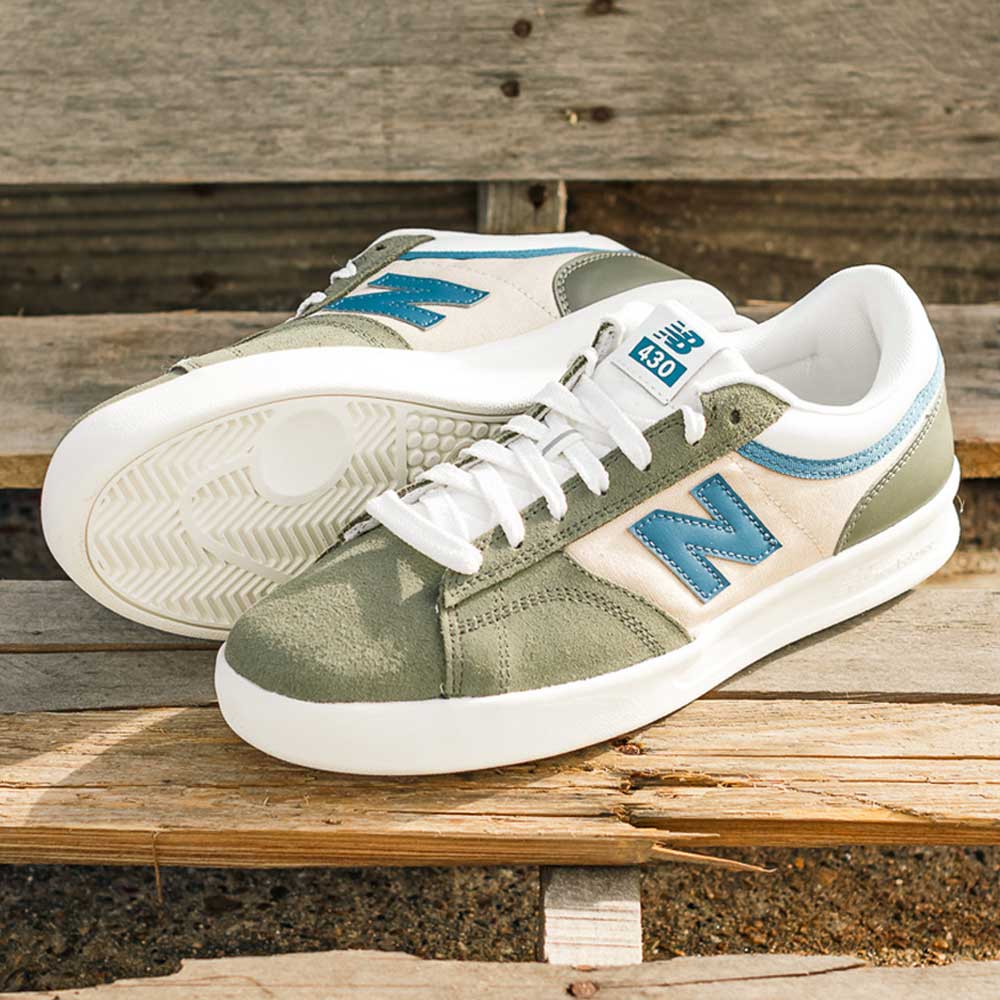 A pair of 430 CZY New Balance Numeric Suede Skateboarding Shoes in blue and green with white laces and cushioned midsole, displayed on a wooden bench outdoors.