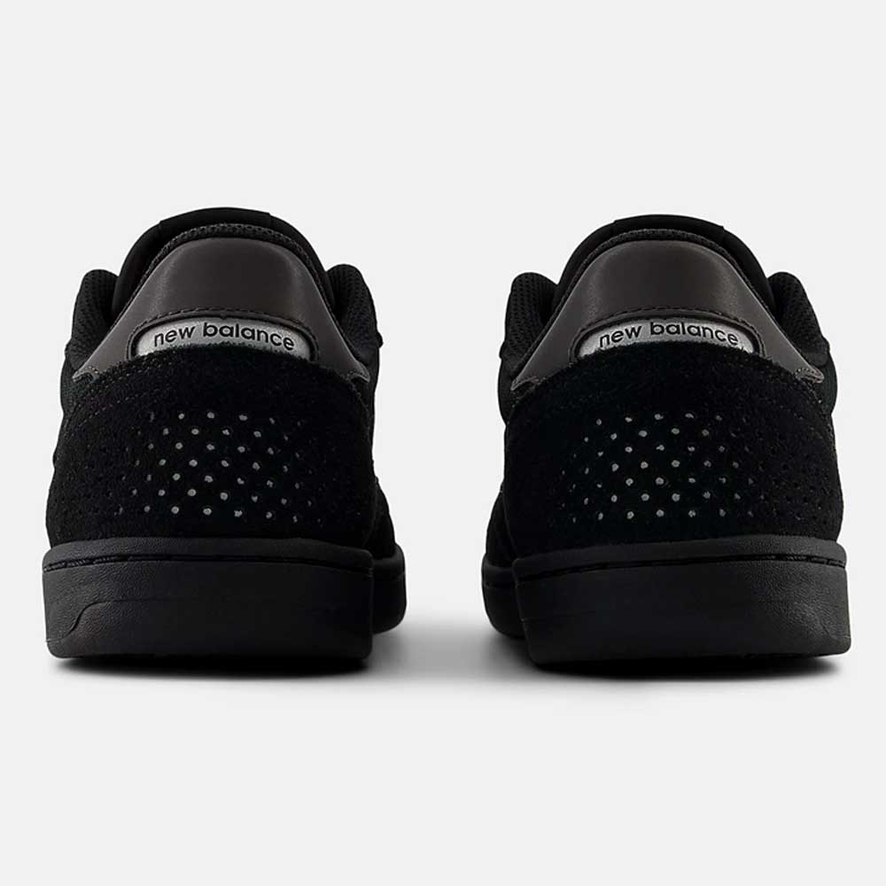 Rear view of a pair of durable black 440 BVU New Balance Numeric Suede Skateboarding Shoes, featuring perforated details and metallic silver New Balance branding on the heels, equipped with an ABZORB midsole for superior cushioning, set against a plain white background.