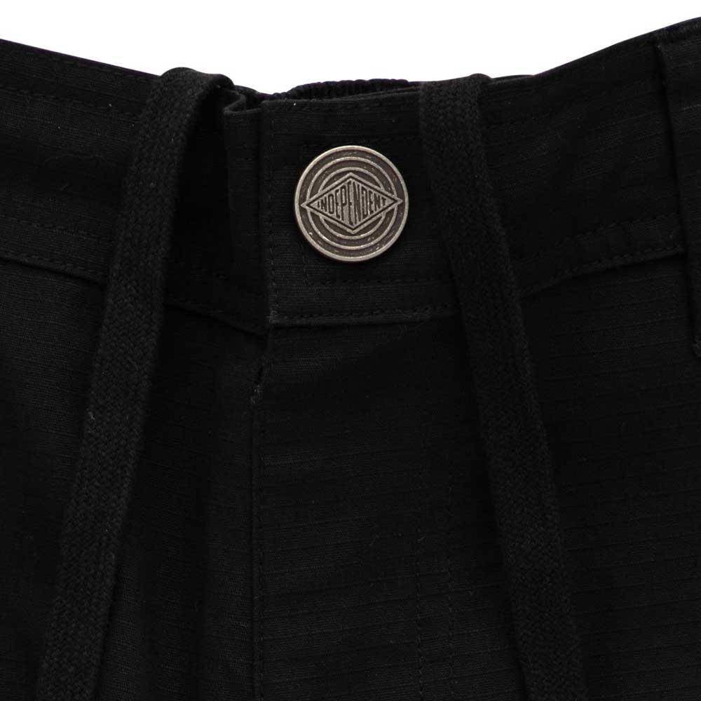 Close-up of the waistband on 44643574 Groundwork Cargo Pants Black Ripstop Bottom Mens Independent, featuring a round metallic button with geometric engraving and text, plus black drawstrings emerging from the waistband.