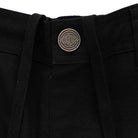 Close-up of the waistband on 44643574 Groundwork Cargo Pants Black Ripstop Bottom Mens Independent, featuring a round metallic button with geometric engraving and text, plus black drawstrings emerging from the waistband.