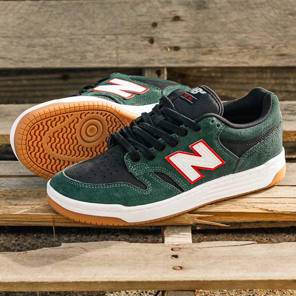 A pair of 480 FOY New Balance Numeric Shoes in suede green and black, featuring white midsoles, gum rubber outsoles, leather overlays, and bold red and white N logos, displayed on a wooden surface.