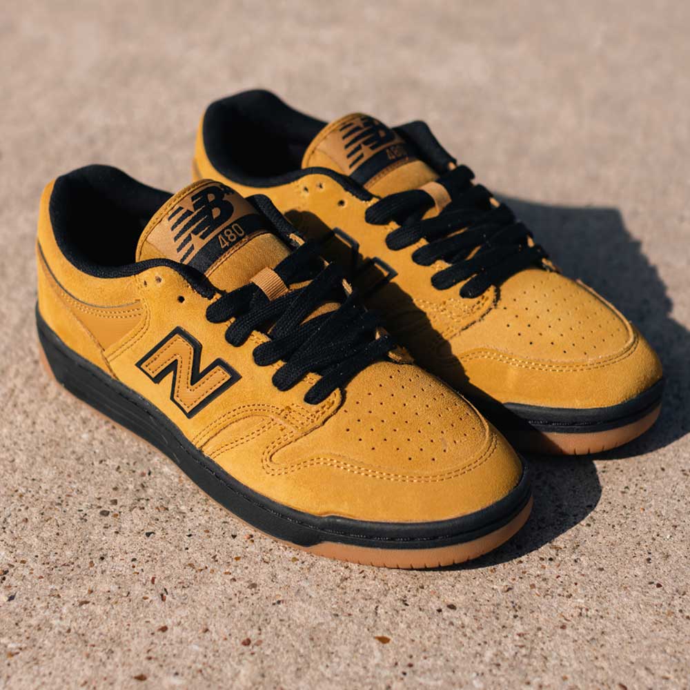 A pair of 480 GDT New Balance Numeric Shoes in Suede Wheat Black with gum soles and black laces rests on a textured concrete surface in sunlight.