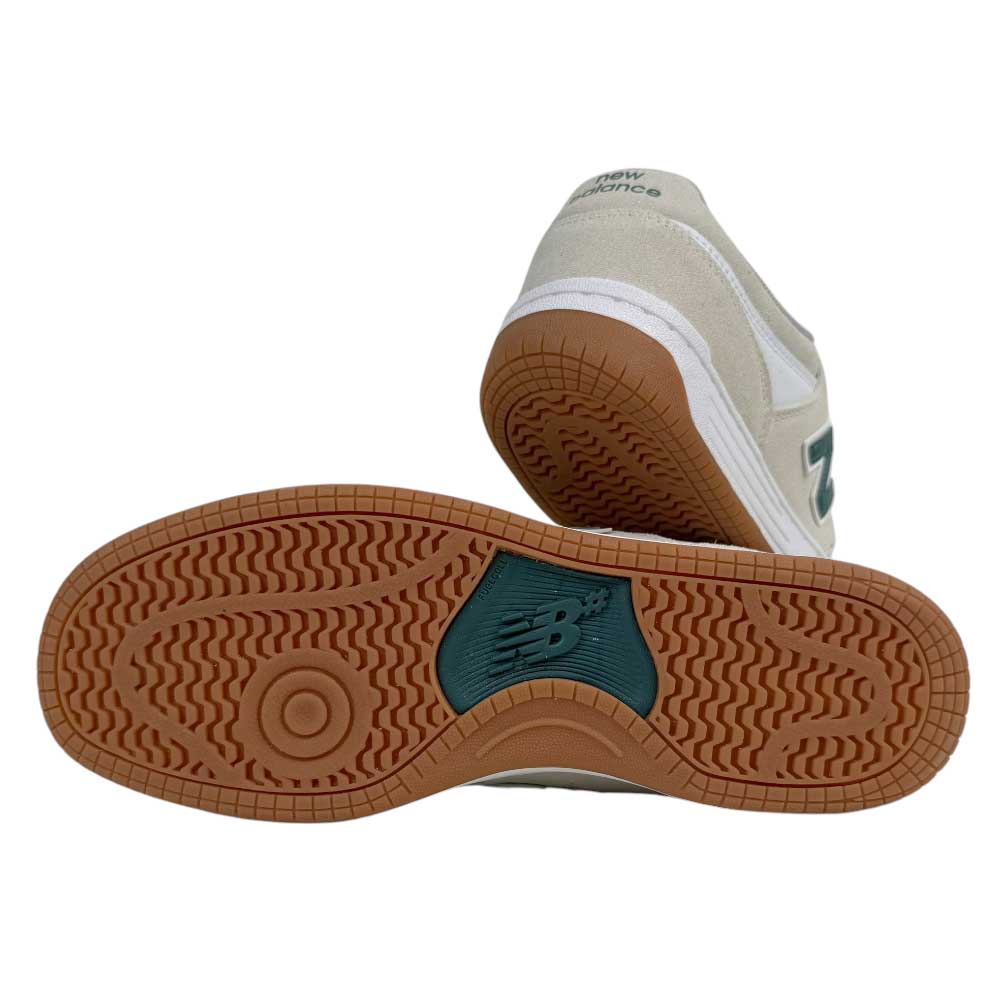 A pair of 480 JDI New Balance Numeric Shoes in Suede White Green, one on its side highlighting the brown rubber sole with New Balance logo, green accents, and a reinforced toe cap; the other shoe stands upright in the background.