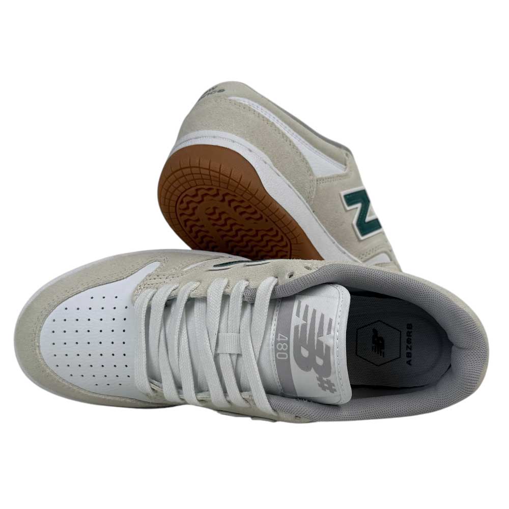 A pair of 480 JDI New Balance Numeric Shoes in suede white and green—one shoe upright showing the top and laces, the other angled to display the brown tread and reinforced toe cap.