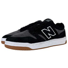 A pair of 480 MGC New Balance Numeric shoes in suede black and dark grey, featuring a durable upper, white midsoles, brown rubber outsoles, and a large white N logo on the side.