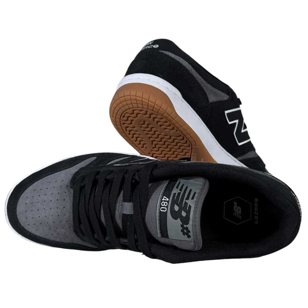 A pair of 480 MGC New Balance Numeric Shoes in Suede Black Dark Grey, featuring a durable upper, white midsoles, and brown outsoles, shown with one shoe upright and the other on its side to display the sole and top design.