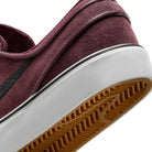 Close-up of the heel and sole on the Janoski GS YOUTH Burgundy Crush Black Suede Nike SB Skateboarding Shoes, featuring a white midsole, gum rubber outsole with black stripe, and detailed tread pattern, shown at a slight tilt.