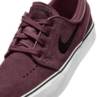 A close-up of the Nike SB Janoski OG 525104607 Burgundy Crush Black suede skateboarding shoe, featuring black laces, a black Swoosh, a white rubber sole with black stripe detail, and responsive Zoom Air cushioning.