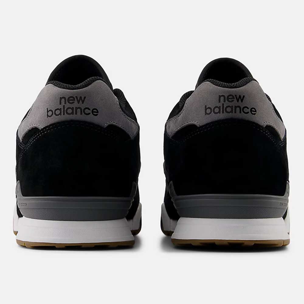 A pair of 770YZZ Black White New Balance Numeric Suede Skateboarding Shoes, viewed from the back on a white background, show black uppers, grey heel tabs with new balance text, white midsoles, and gum rubber outsoles for court stability.
