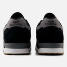 A pair of 770YZZ Black White New Balance Numeric Suede Skateboarding Shoes, viewed from the back on a white background, show black uppers, grey heel tabs with new balance text, white midsoles, and gum rubber outsoles for court stability.