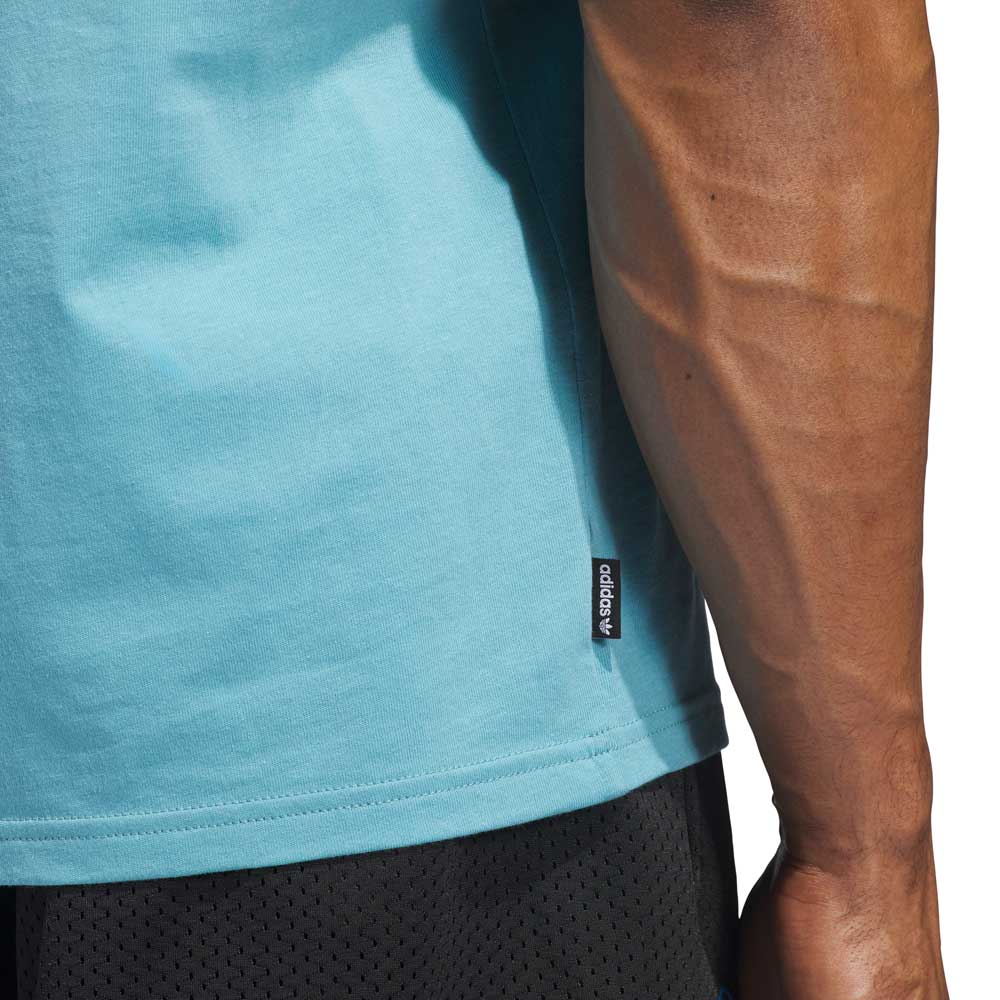 A close-up of a muscular arm and torso in the Kogan Logo Tee Blue Black KC6301 by Adidas Skateboarding, an ideal action sports tee with signature seam tag, paired with black mesh shorts.