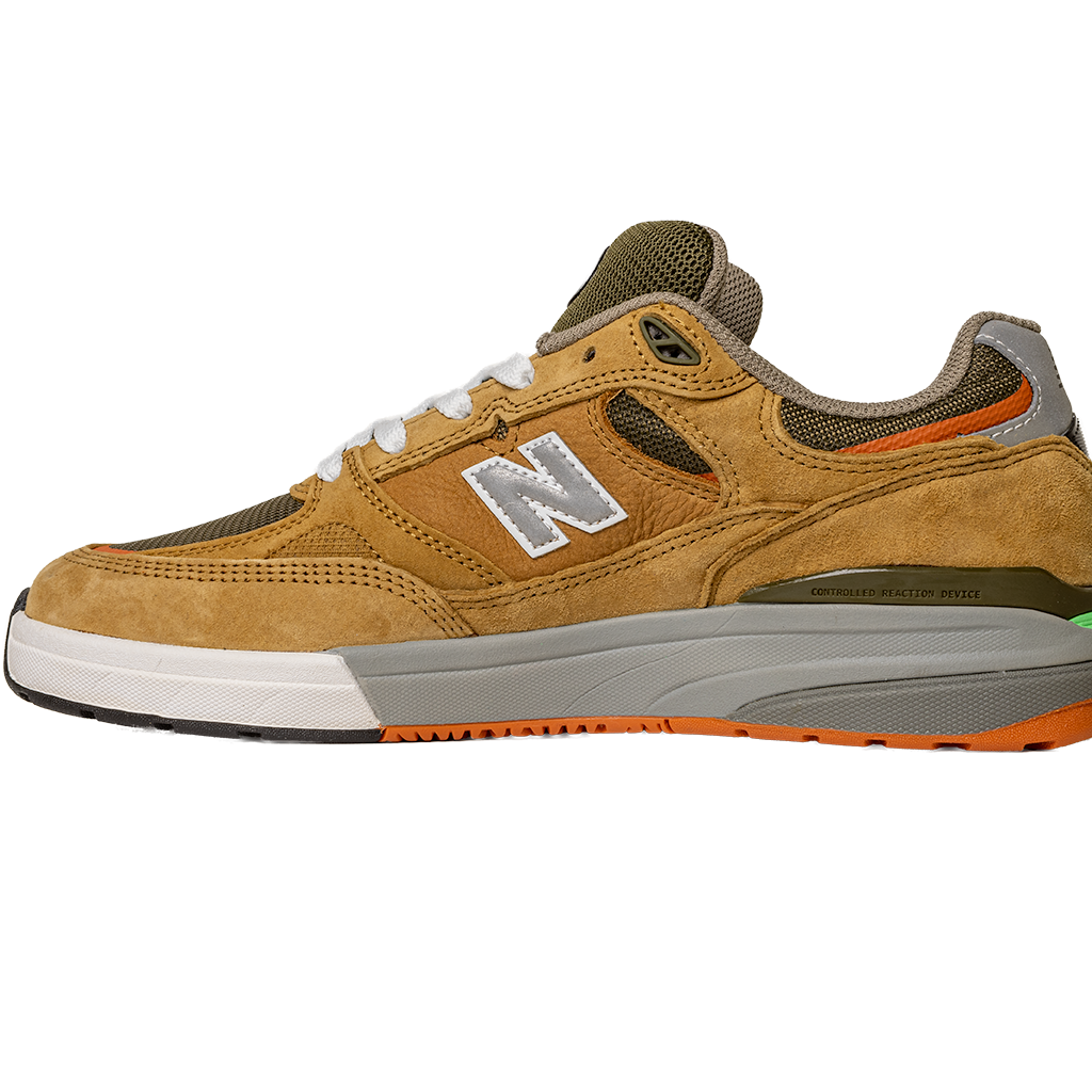 The 933 MNO Andrew Reynolds Brown Grey New Balance Numeric Skateboarding Shoes feature suede, mesh upper, white laces, a white and silver N logo, orange sole detail, and green heel accents—shown in side profile on a white background.