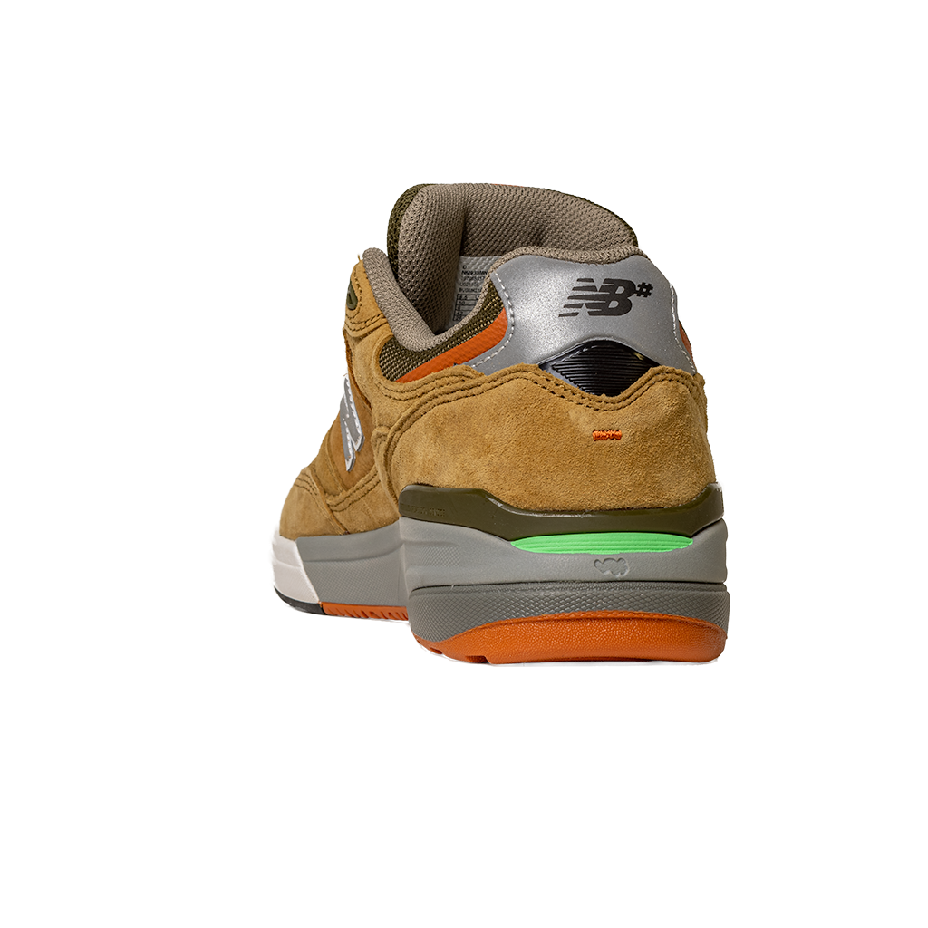 The 933 MNO Andrew Reynolds Brown Grey New Balance Numeric Skateboarding Shoe features tan suede, a gray heel with the New Balance logo, a green accent above the sole, and an orange outsole, shown from the back on a white background.