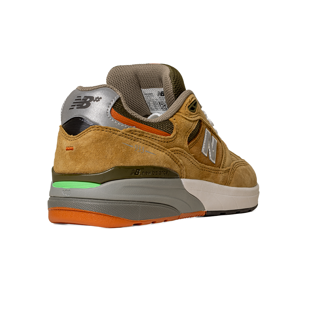 The 933 MNO Andrew Reynolds Brown Grey New Balance Numeric Skateboarding Shoes Suede feature a tan suede upper, silver heel with logo, grey midsole, orange outsole, and green accents above the heel, shown from the back angle.