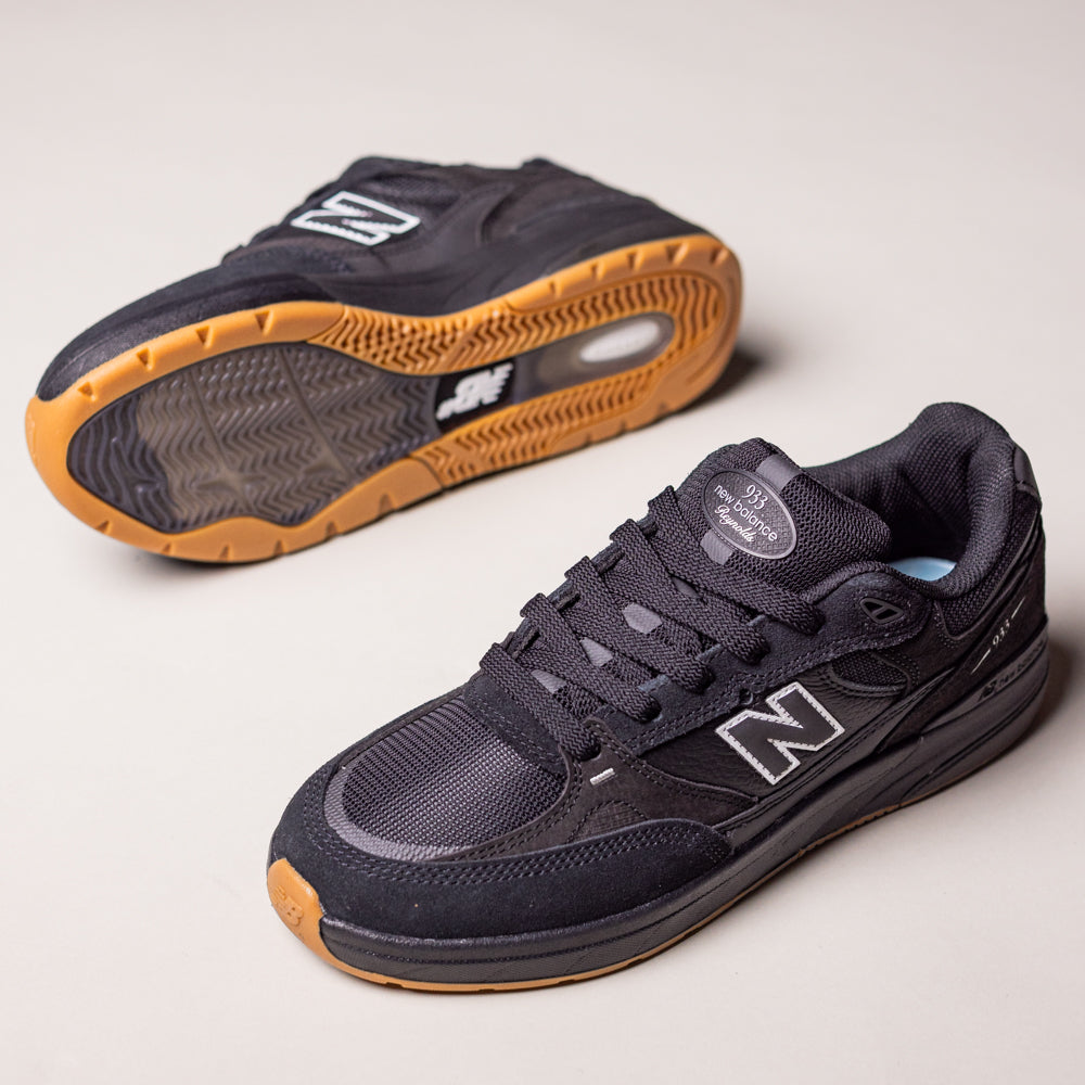 A pair of Black 933 NAP New Balance Numeric Suede Skateboarding Shoes is displayed on a light background—one upright showing the side and laces, the other on its side highlighting the gum sole and tread pattern.