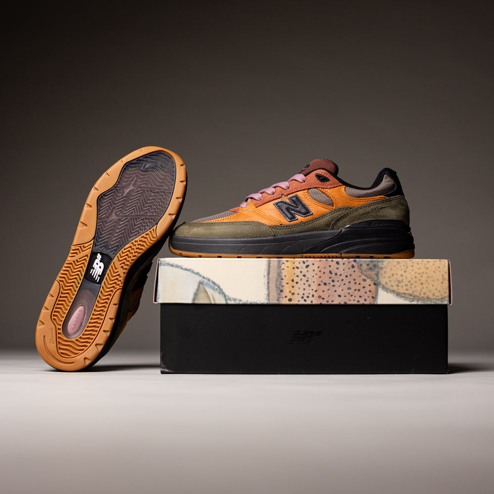 A pair of Mike Gigliotti True Brown Candy Pink 933 LOT New Balance Numeric suede skateboarding shoes with premium cushioning—one shoe stands on a nature-inspired shoebox, the other leans to display its sole and highlight their stylish heritage design.