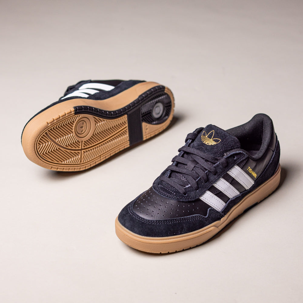 A pair of Black White Gum Tyshawn 2 II HQ4734 Adidas Skateboarding Shoes, featuring white stripes and gum soles, is displayed on a light beige background—one shoe upright and the other showing the sole.