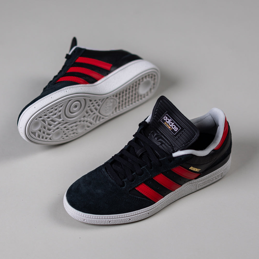A pair of JH8606 Black Betsc Busenitz Adidas Skateboarding Suede Shoes with red stripes and white soles; one shoe stands upright showing the side, while the other is on its side highlighting the patterned sole and brand logo on the tongue.