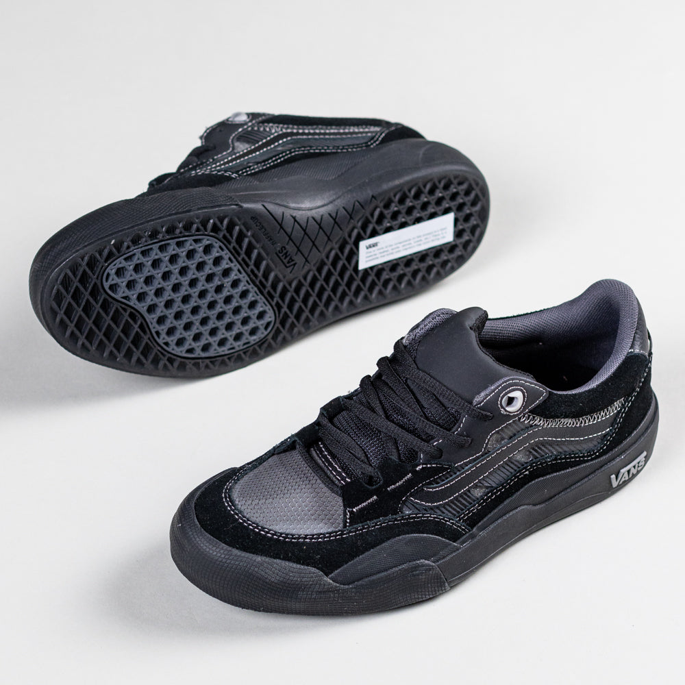 The VN000D5D1741 Wayvee Skate 2 Black Black Grey Vans feature black suede and mesh, black soles and laces. One shoe stands upright while the other lies on its side, displaying a hexagonal grip pattern for durable skateboarding.