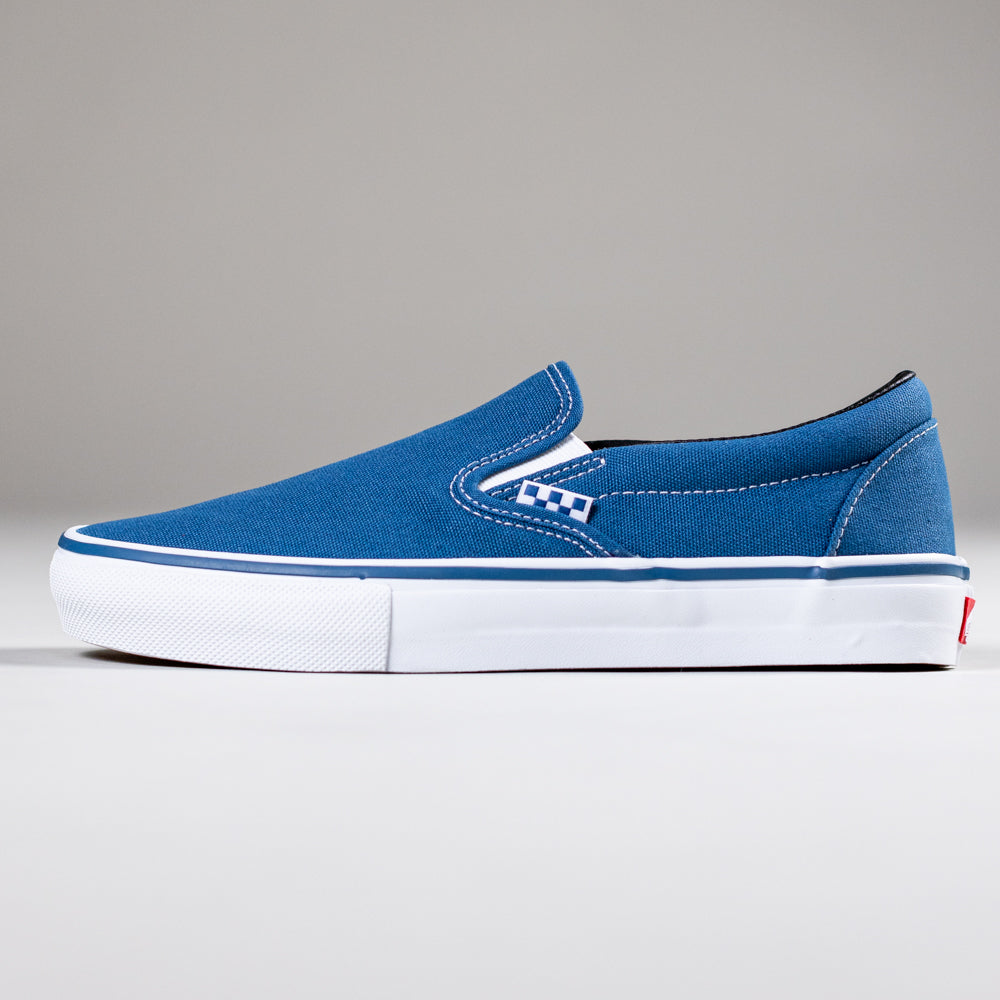 The VN0A5FCANVY1 Navy Skate Slip On Vans Canvas Shoes feature a blue canvas upper, white rubber sole, DURACAP reinforcement, and a checkered tag by the elastic side panel, displayed in profile on a plain gray background.
