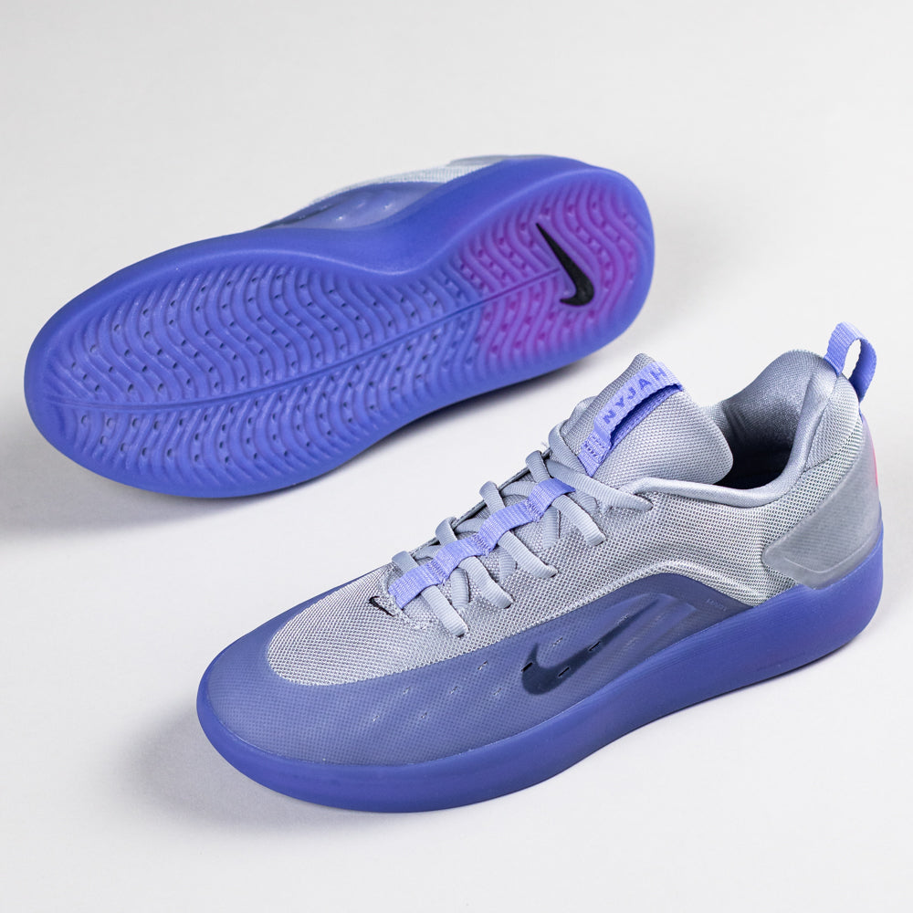 A pair of FQ1273500 Light Thistle Black Zoom Nyjah 4 Nike SB skateboarding shoes with reinforced mesh uppers, translucent purple-blue Air Zoom soles, and black Nike swooshes. One shoe stands upright; the other lies on its side, showing the sole.