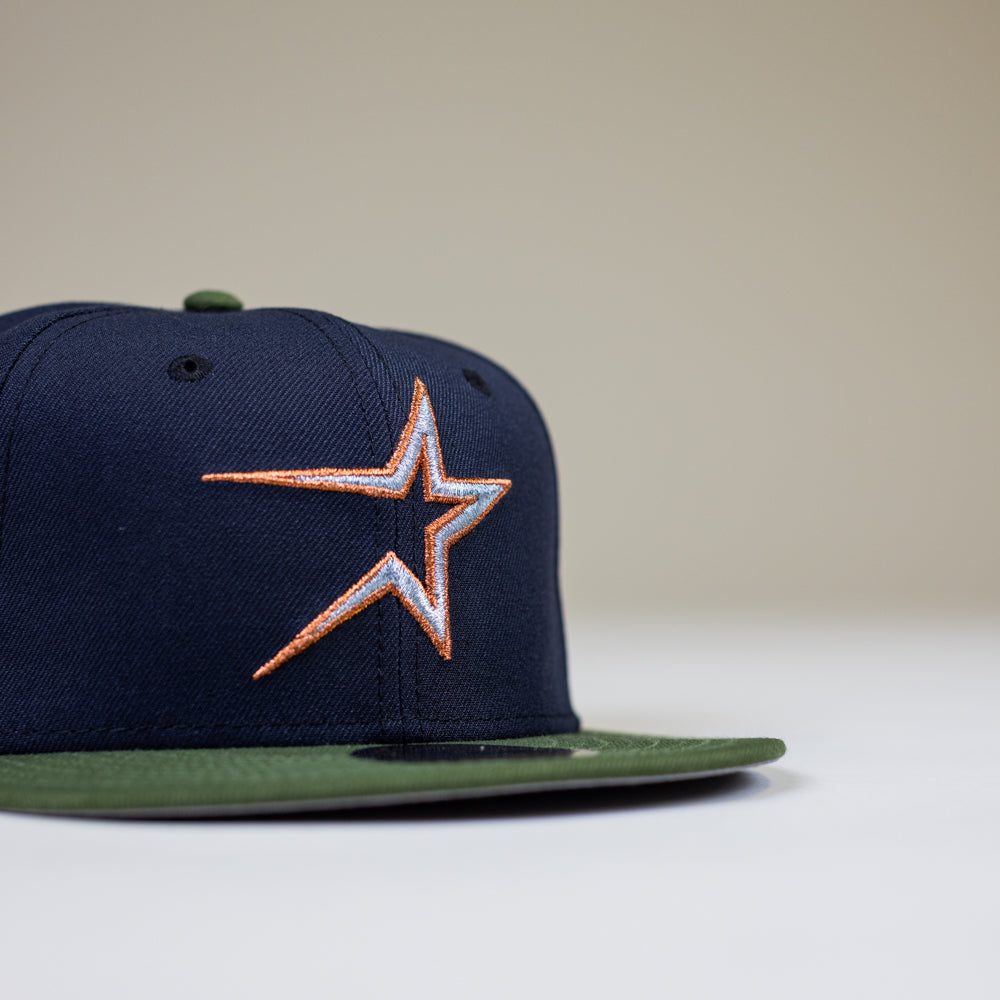 The Aquamarine Navy Rifle Green Astros New Era Hat 5950 Fitted, featuring an orange and white star logo on the front, is shown against a plain light background.