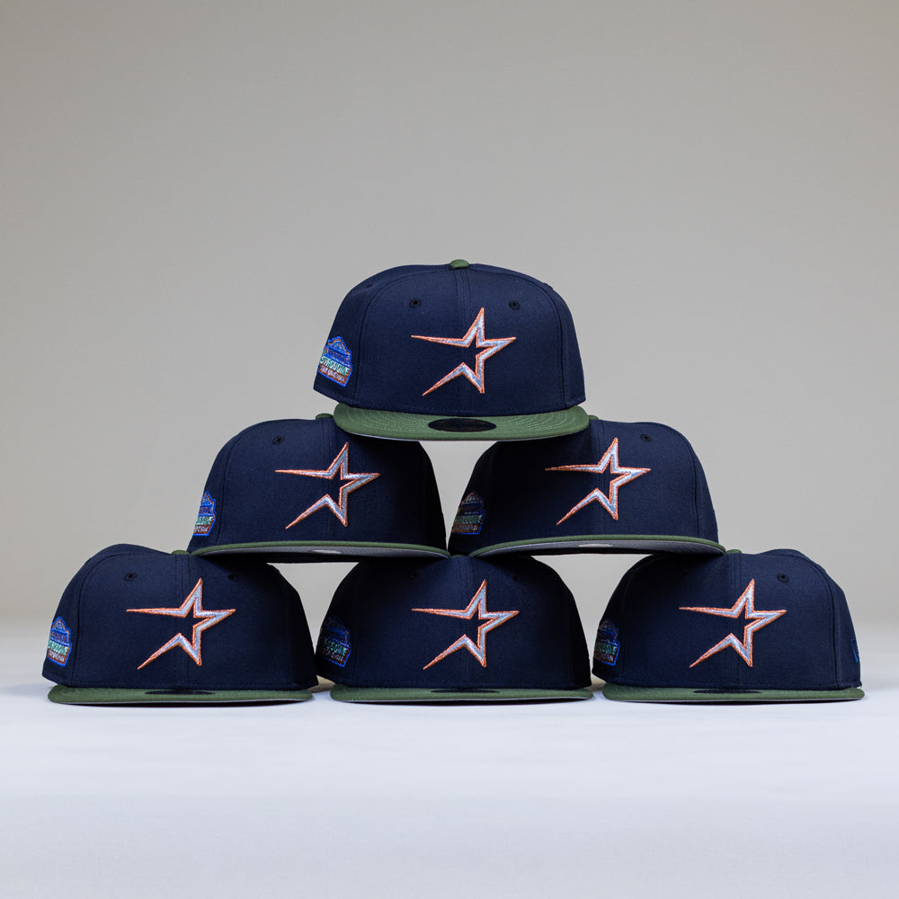 Six Aquamarine Navy Rifle Green Astros New Era Hat 5950 Fitted caps with orange star logos and green brims are arranged in a pyramid on a white surface. These fitted caps also feature a side patch for a classic, bold look.
