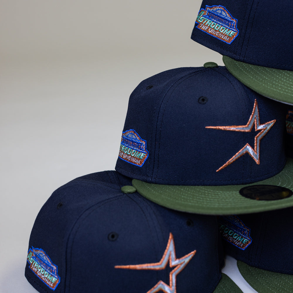 A stack of Aquamarine Navy Rifle Green Astros New Era 5950 Fitted hats, each with a star logo on the front and a colorful "713 OG CAP THE ORIGINAL" patch on the side.