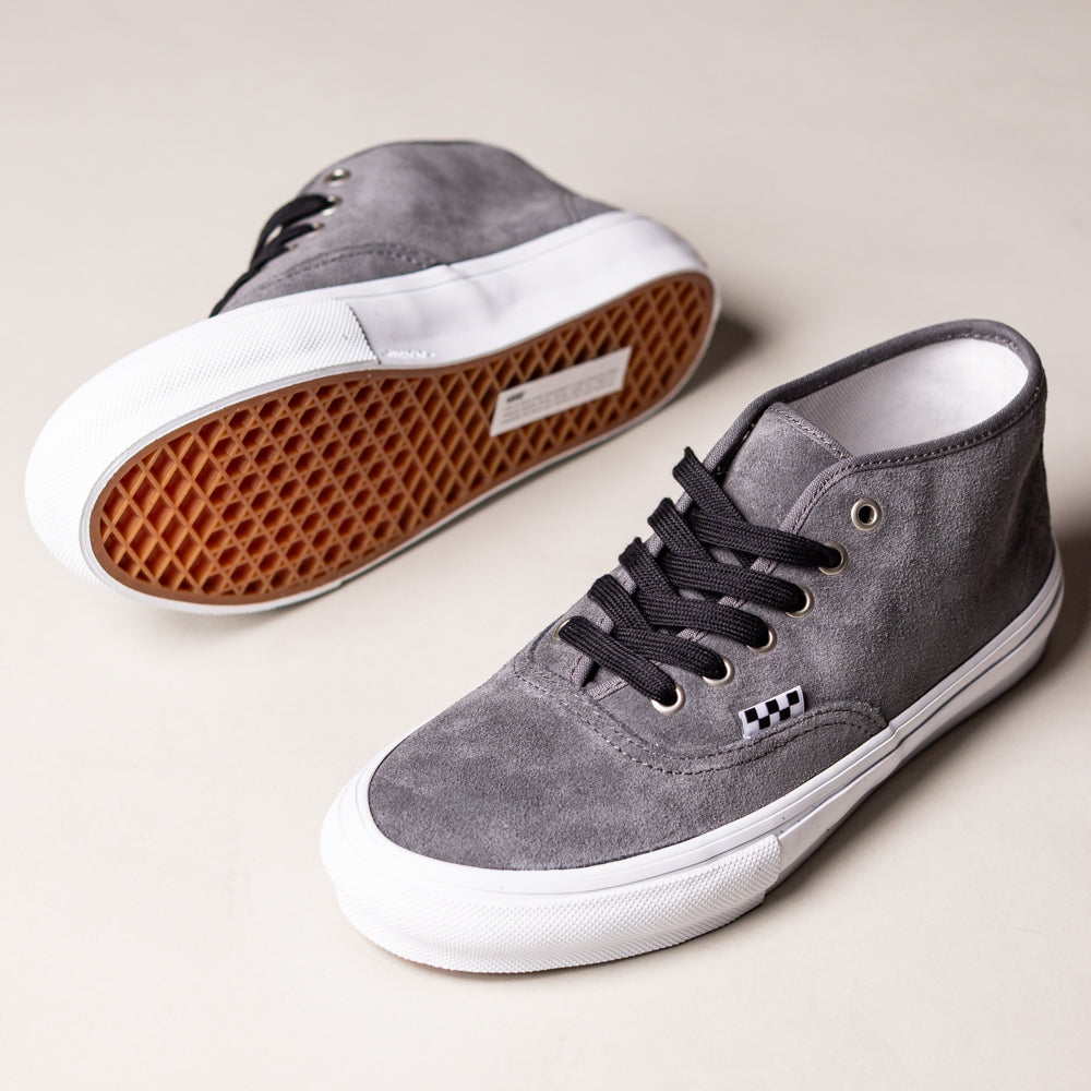 A pair of Vans Skate Authentic Mid VN000EJSPWT1 Pewter Suede skateboarding shoes with black laces and white rubber soles—one upright, one on its side showing the brown waffle outsole—rest on a light surface.