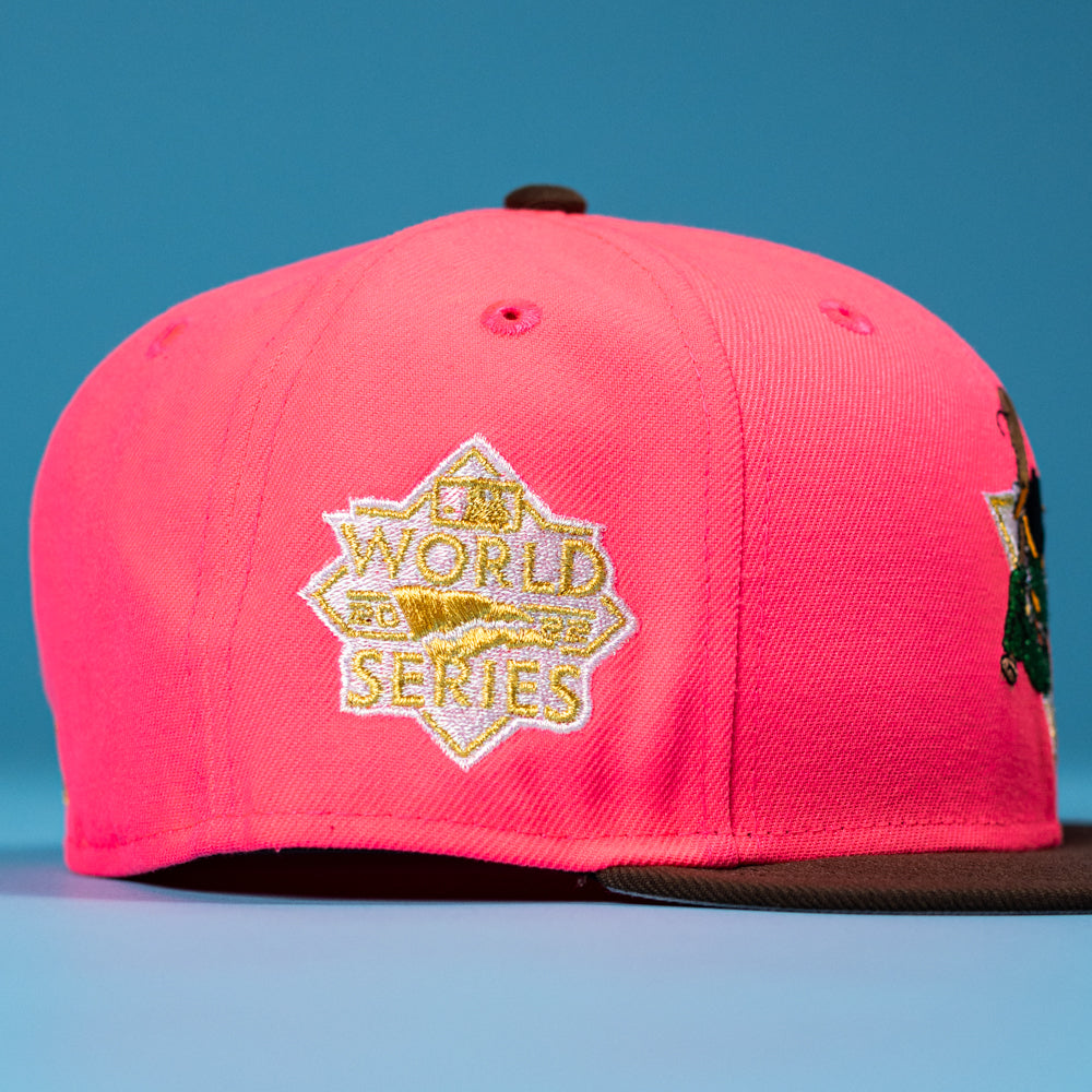 A close-up of the Pink Comet WS22 Houston Astros 5950 Fitted New Era Hat with a black brim and embroidered gold and white World Series emblem on the side, set against a solid blue background.