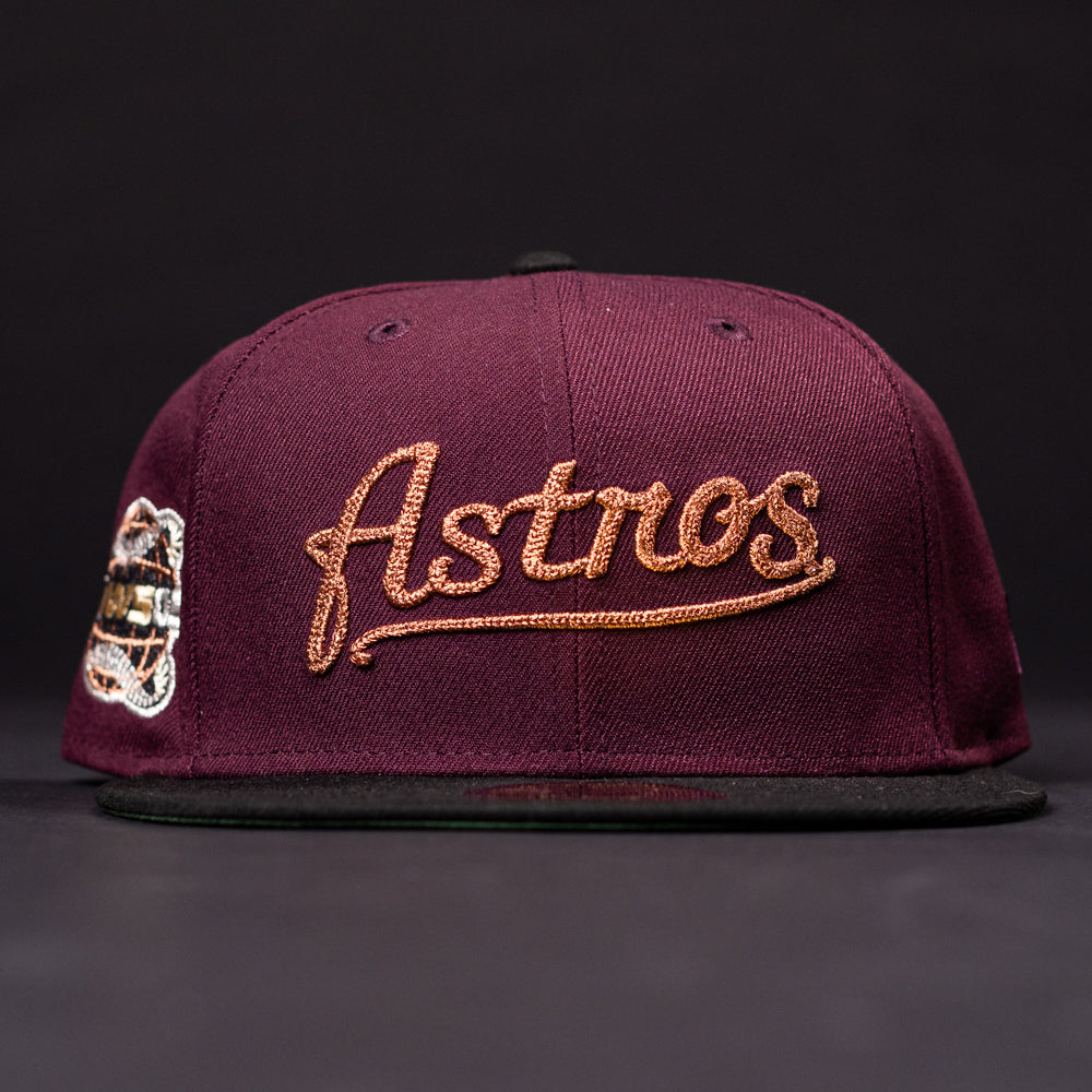 The 05 Debut Maroon Black Houston Astros New Era Hat 5950 Fitted features gold script "Astros" embroidery on the front and a commemorative patch on the left side, shown against a dark background.
