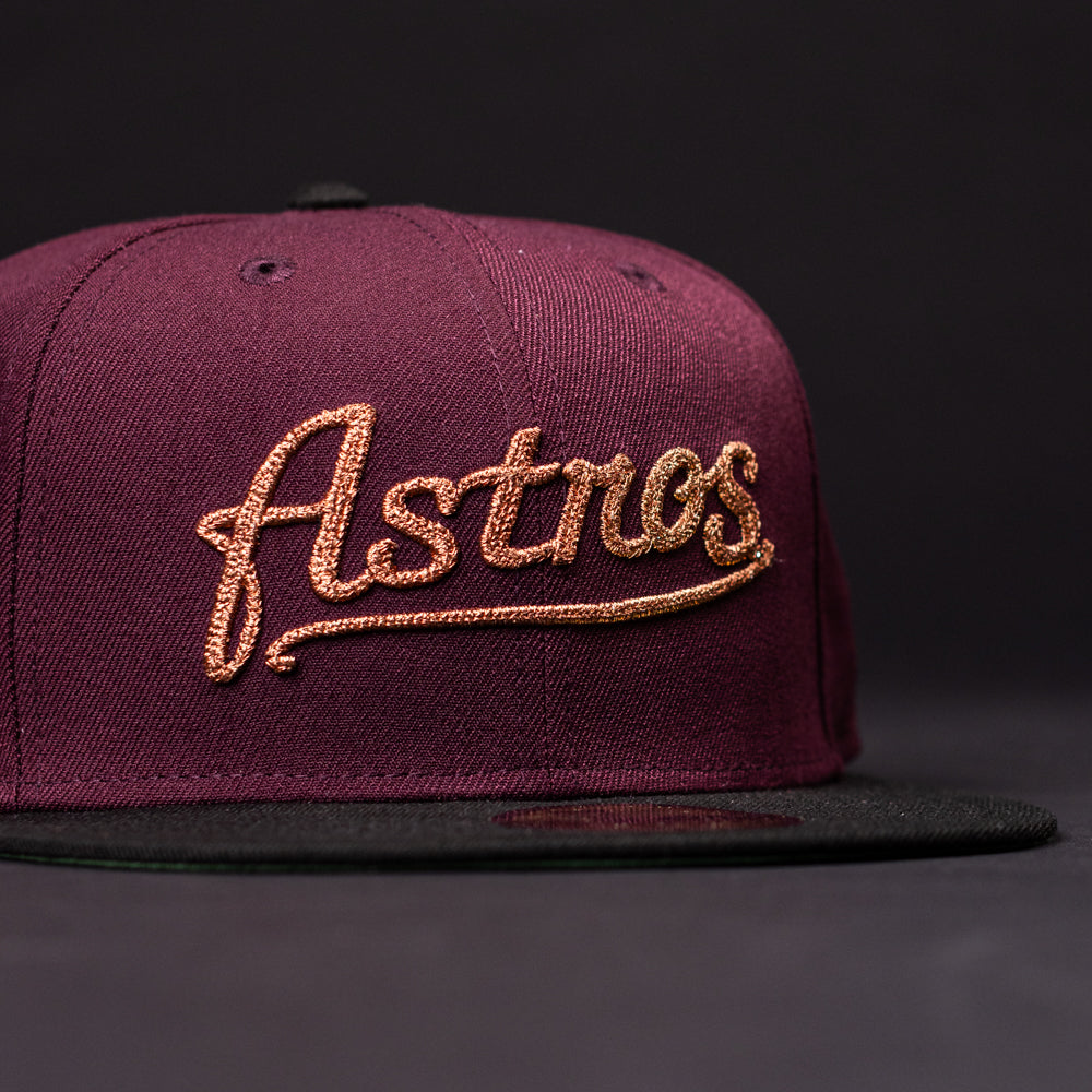 The 05 Debut Maroon Black Houston Astros New Era Hat 5950 Fitted features "Astros" in gold script on the front, a maroon crown, and a black flat brim, styled against a dark background.
