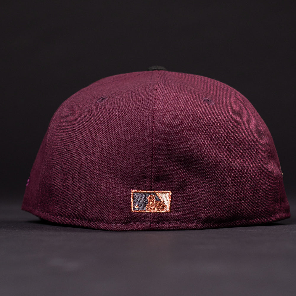 The 05 Debut Maroon Black Houston Astros New Era Hat 5950 Fitted is shown from the back, displaying a small embroidered MLB logo in white, blue, and gold near the bottom edge. The hat sits on a dark surface against a black background.