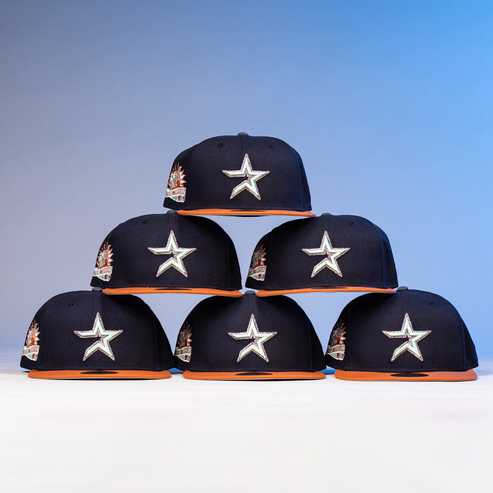 Six “The Feast Navy Rust Houston Astros New Era Hat 5950 Fitted” caps are stacked in a pyramid. Each New Era hat has a navy crown, rust brim, large white star logo on the front, and a colorful patch on the side, over a gradient blue background.