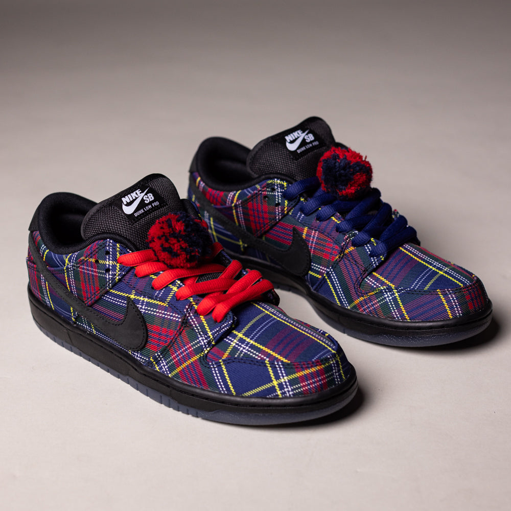 The READ BELOW the BUTTON RAFFLE Nardwuar Nike SB Dunk Low Pro features blue, red, and yellow plaid, mismatched laces, and a pom-pom on the right tongue—ideal for your next Southside Skatepark raffle entry.