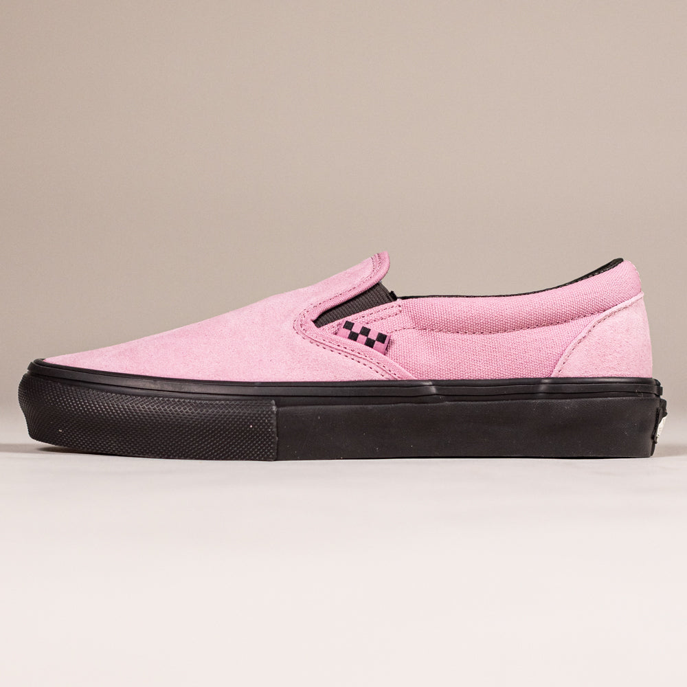 The VN0A5FCAPIB1 Pink Black Skate Slip On Vans Suede Shoes feature pink suede, black accents, a black sole, and a small black and white checkerboard by the elastic side. Designed for durability and board control, shown on a beige background.