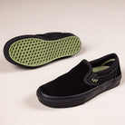 The VN000EKPGSH Black Black Olive Skate Slip On Vans Suede Shoes feature black uppers, black midsoles, white stitching, and green waffle-patterned soles, shown on a light background with one shoe upright and one on its side for display.