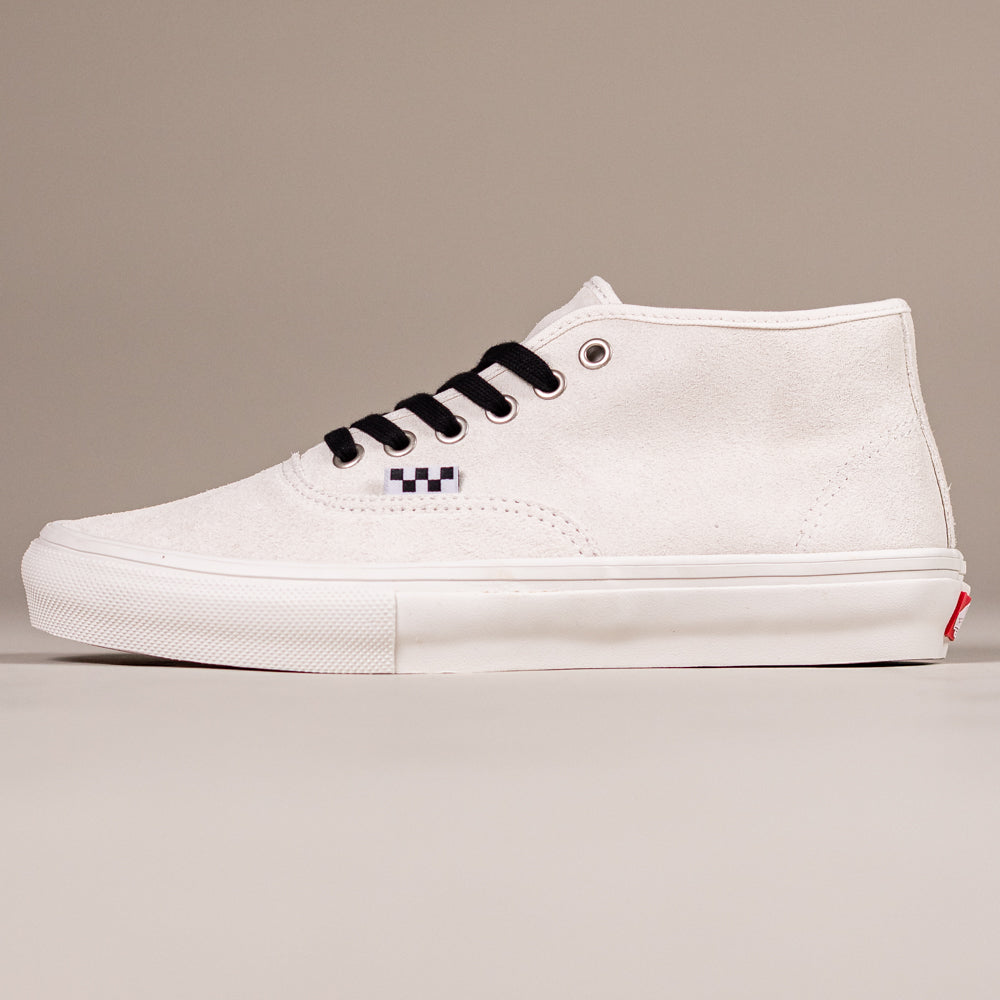 The VN000EJSJVY Blanc de Blanc Authentic Mid Vans Skate Suede Shoes feature white suede, black laces, a black and white checkerboard detail, a white rubber sole with waffle outsole, and a red heel logo tag, shown on a beige background.