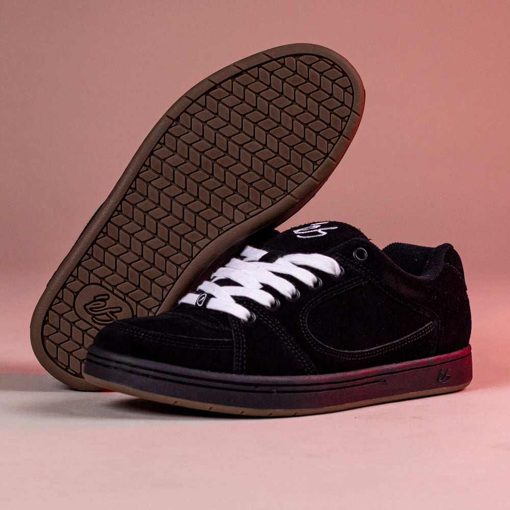 A pair of Accel Black Noir Es Shoes Skateboarding Original Shape is shown on a pink background: one upright, the other displaying its brown patterned sole and white laces, highlighting the classic cupsole skate shoe design.