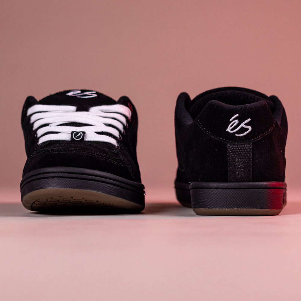 A pair of Accel Black Noir Es Shoes Skateboarding Original Shape with white laces and the éS logo, shown front and back on a soft pink background—iconic 1995 classic cupsole skate shoes.
