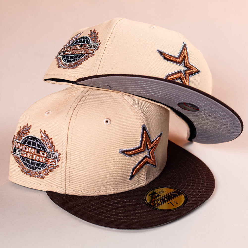 Two Flat White WS05 Mango Wood Astros New Era Hat 5950 Fitted caps, featuring embroidered star logos and World Series patches, are stacked on a light background—one upright showing the front, the other upside down displaying the underside of the bill.