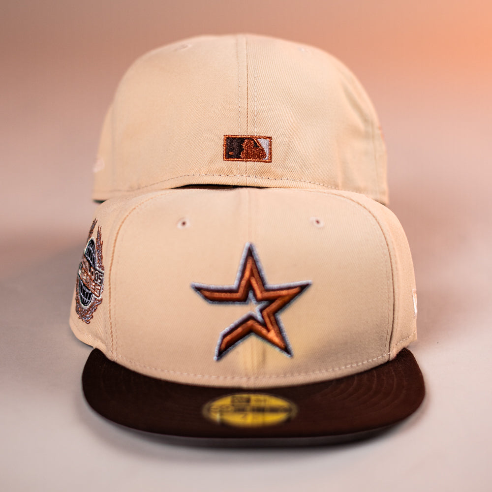 Two Flat White WS05 Mango Wood Astros New Era Hat 5950 Fitted caps are shown: one faces forward, the other backward. The front cap has a brown star logo, a commemorative side patch, and a dark brown brim.