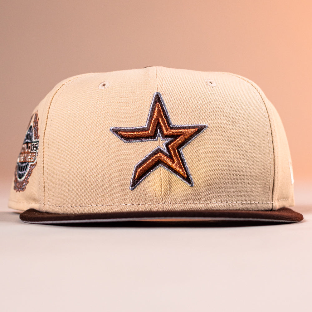 The Flat White WS05 Mango Wood Astros New Era Hat 5950 Fitted features an outlined orange and black star logo on the front, a colorful patch on the left, and a brown brim, all set against a soft peach beige background.
