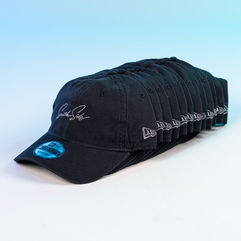 A row of identical Southside Pewter Script Strapback 920 Hats by New Era, each with white embroidery on the front and side, are neatly lined up diagonally against a blue and white gradient background.
