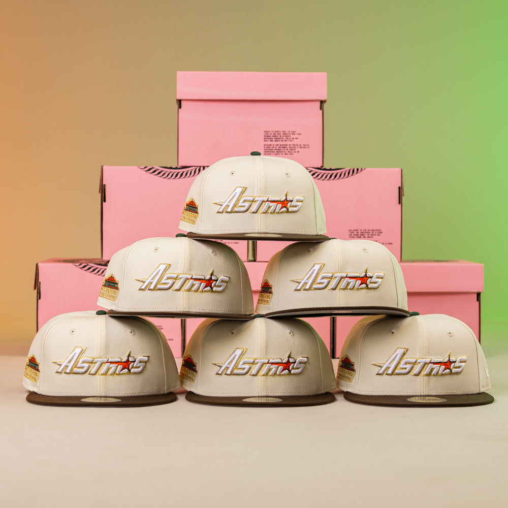 A stack of hats, featuring the Oompa Pink Box Houston Astros New Era Hat 5950 Fitted, with a pink box behind them.