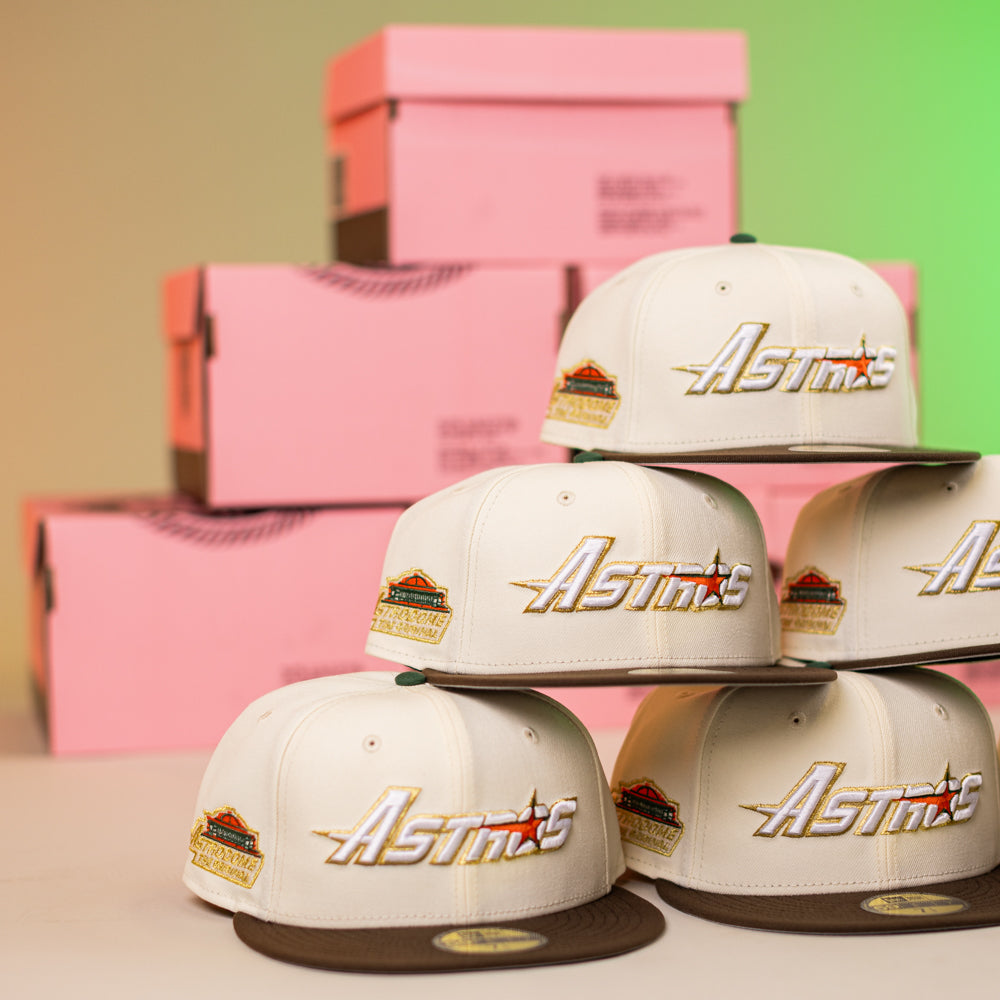 Five Oompa Pink Box Houston Astros New Era Hat 5950 Fitted caps are stacked in two rows, with pink shoe boxes behind them against a green and beige gradient wall.