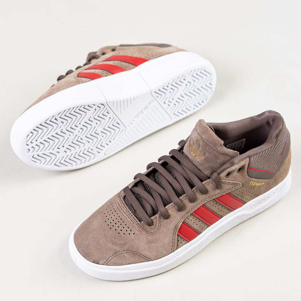 A pair of JR9499 Earth Color Tyshawn Adidas Skateboarding Suede Shoes with red stripes, white cupsoles, and gold Tyshawn branding are displayed on a white background; one shoe stands upright, the other is on its side.